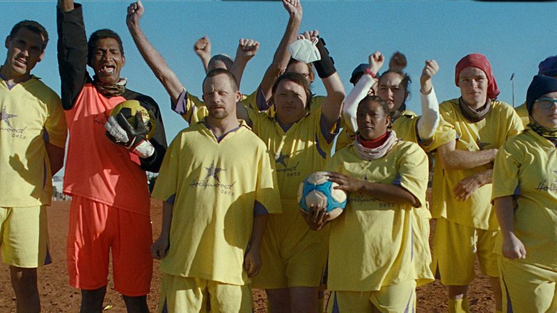 A football team celebrating in front of the camera. They are wearing a yellow football kit.